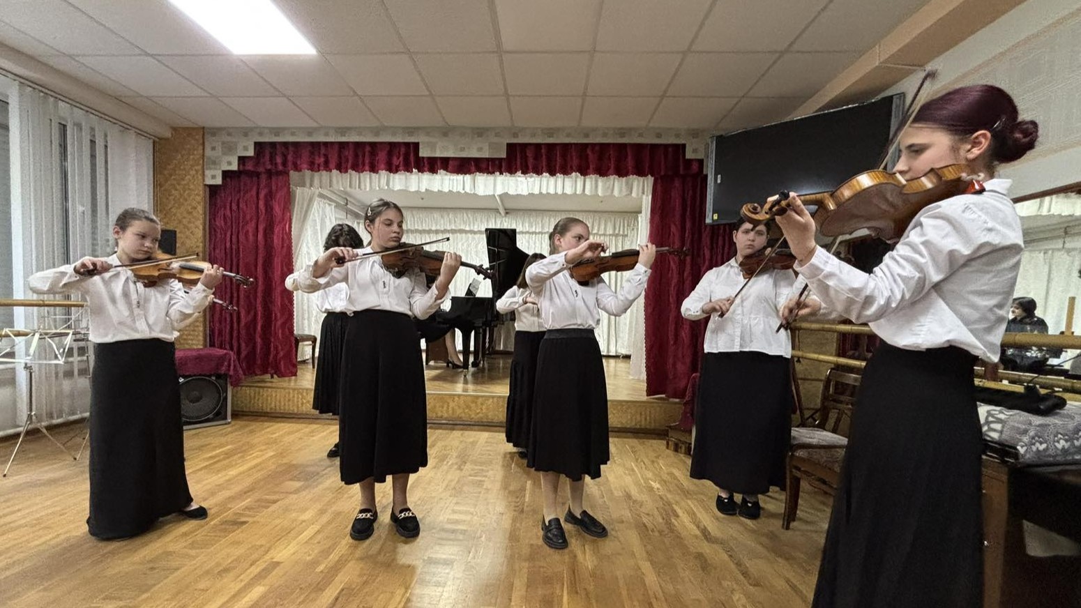 Пʼять дівчат репетирують зі скрипками в концертній залі