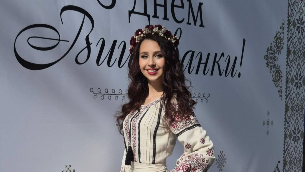 Жінка у вишиванці стоїть біля банера до Дня вишиванки